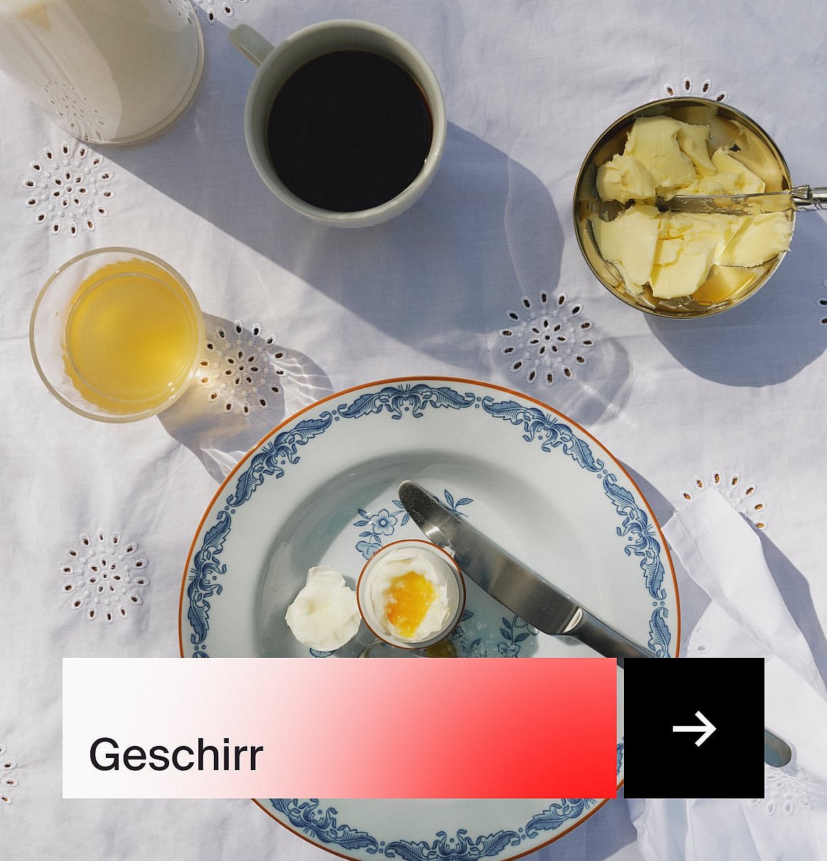 Frühstück von oben gesehen: Kaffee, Saft, weichgekochtes Ei, Butter und ein gemusterter Teller auf einer weißen, bestickten Tischdecke.