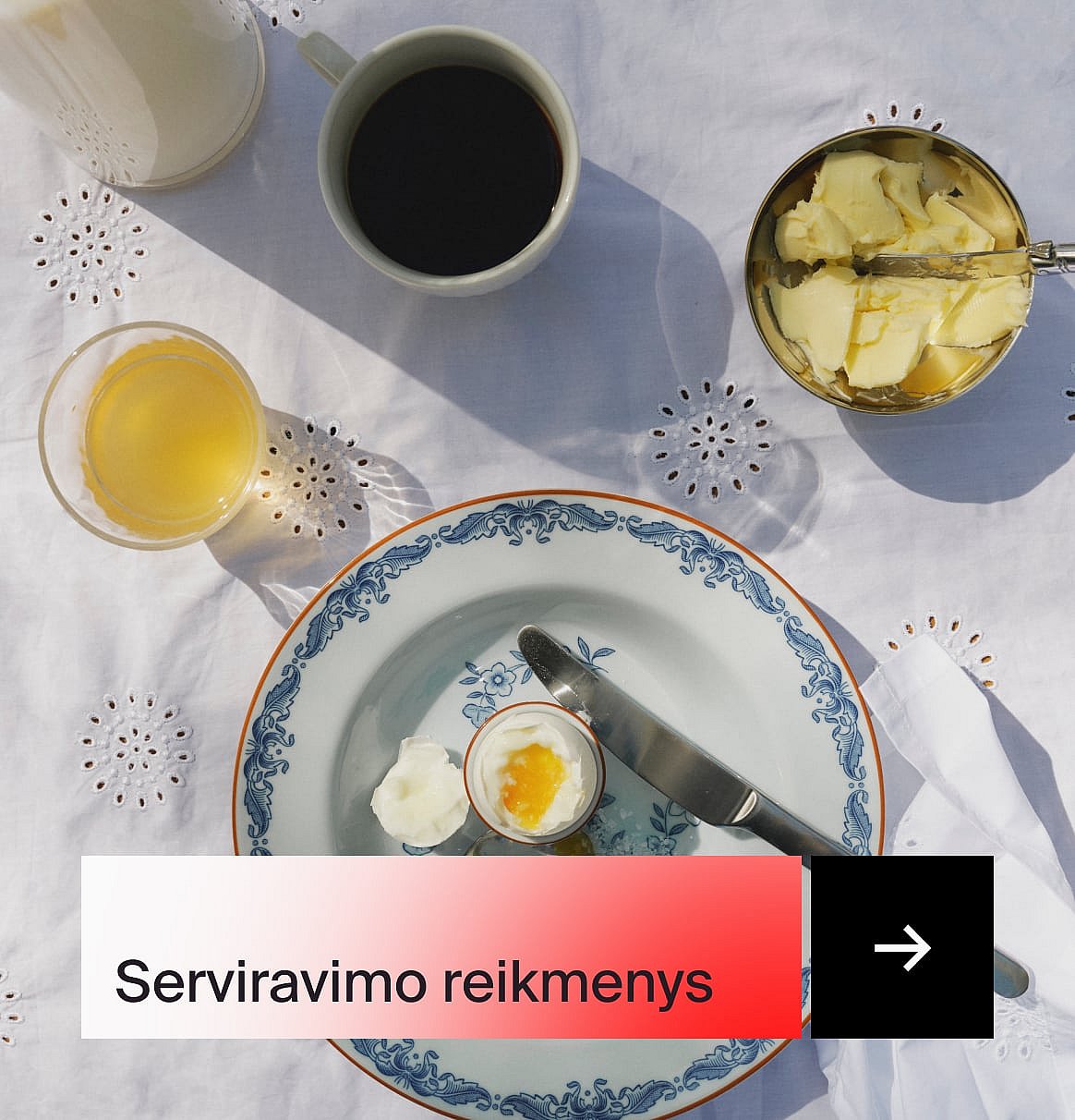 Pusryčiai: kava, sultys, minkštai virtas kiaušinis, sviestas ir raštuota lėkštė ant baltos išsiuvinėtos staltiesės.
