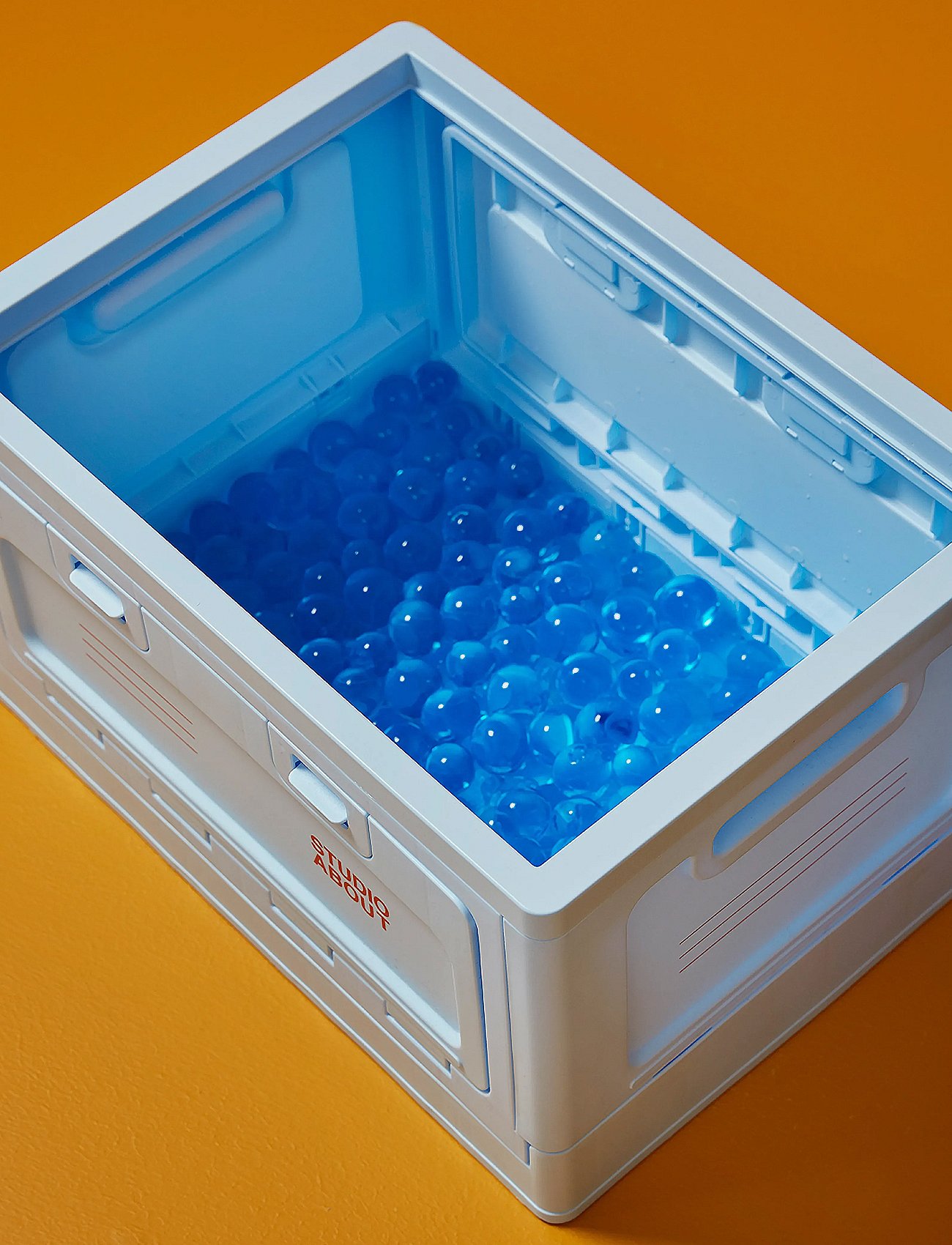 White plastic crate filled with blue translucent spheres, on an orange background.