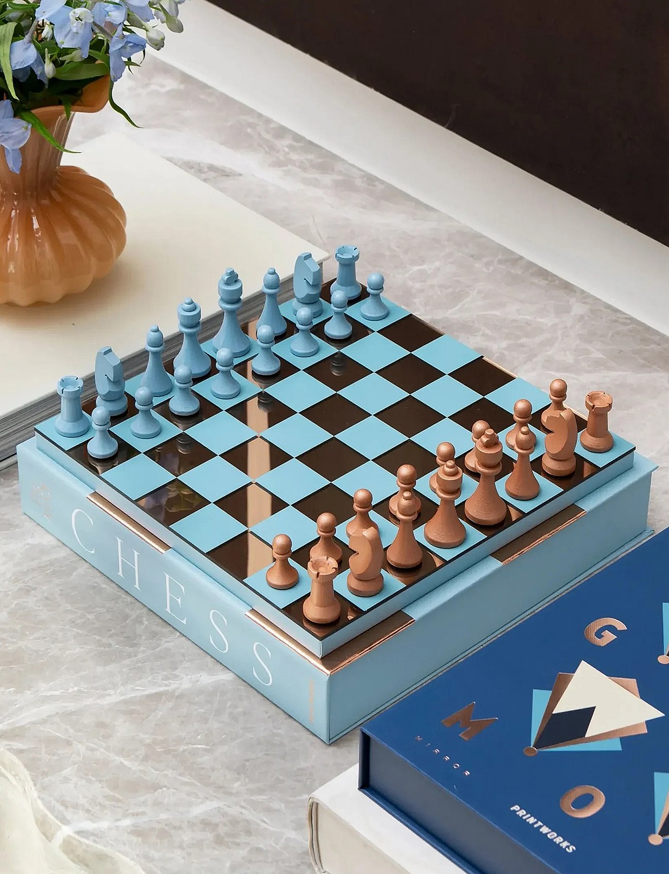 Light blue and copper chess pieces arranged on a light blue and mirrored board, on a marble table.