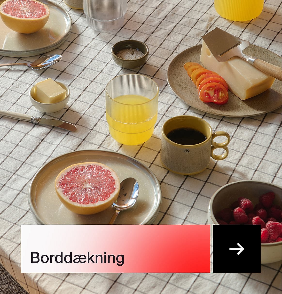 Et morgenmadsbord med grapefrugt, juice, kaffe, ost, tomater, smør og hindbær på en ternet dug.