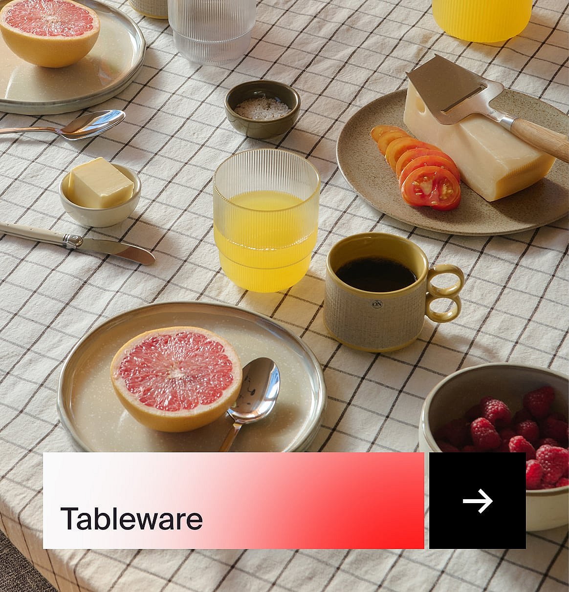 Breakfast table with grapefruit, juice, coffee, cheese, tomatoes, butter, and raspberries on a checkered tablecloth.