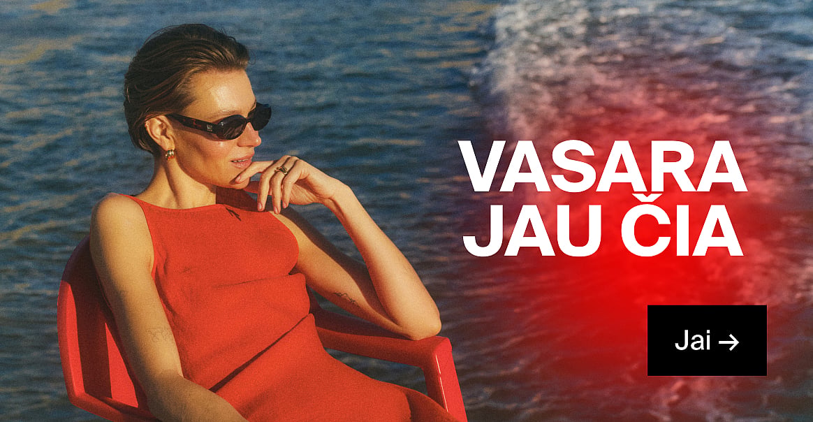 Moteris raudona suknele ir akiniais nuo saulės, ranka prie smakro, stovi prie mėlyno vandens. Užrašai: „VASARA JAU ČIA“ ir „Jai →“.