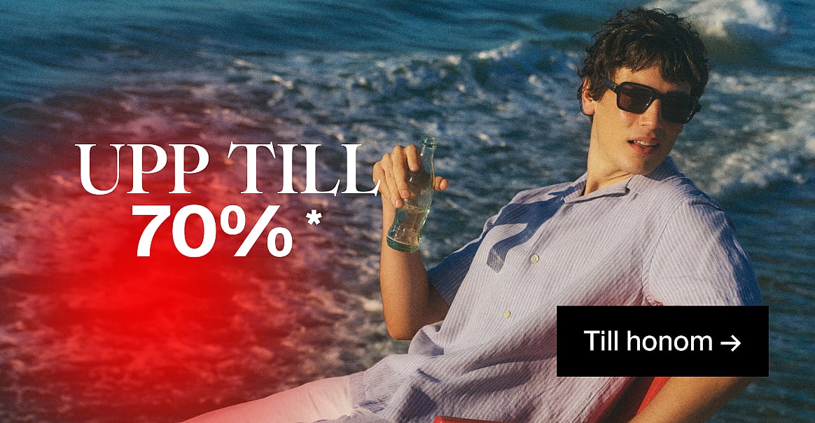 En man i solglasögon och randig skjorta, med en flaska i handen, vid havet. Text: UPP TILL 70% RABATT, För honom.*