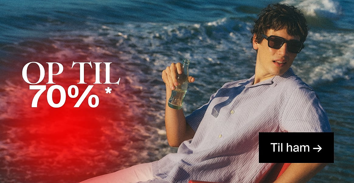 Mand i solbriller og stribet skjorte, der holder en flaske, ved havet. Tekst: OP TIL 70% RABAT, Til ham.*