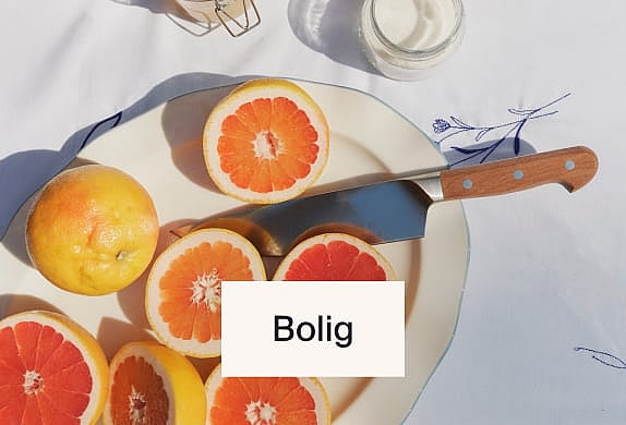 Skivede og hele grapefrugter på en hvid tallerken med en kniv, på en hvid dug. Klart, naturligt lys.