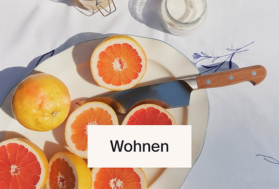 In Scheiben geschnittene und ganze Grapefruits auf einem weißen Teller mit einem Messer, auf einer weißen Tischdecke. Helles, natürliches Licht.