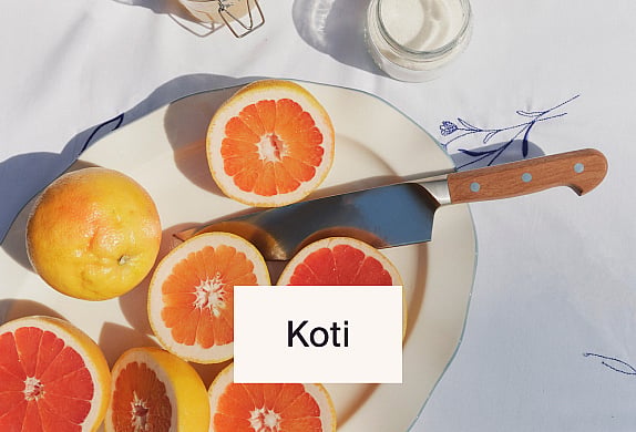 Viipaloituja ja kokonaisia greippejä valkoisella lautasella veitsen kera, valkoisen pöytäliinan päällä. Kirkas, luonnonvalo.