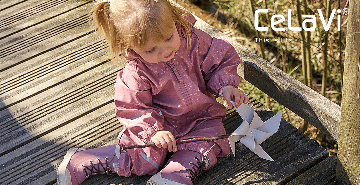 Young child with dark curly hair and a pink embroidered top, looking right, outdoors.