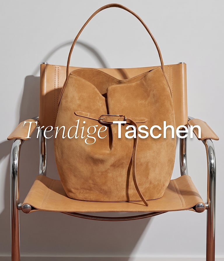 Eine hellbraune Wildleder-Beuteltasche auf einem hellbraunen Leder- und Chromstuhl vor einer weißen Wand. Textüberlagerung: „Trendige Taschen“.