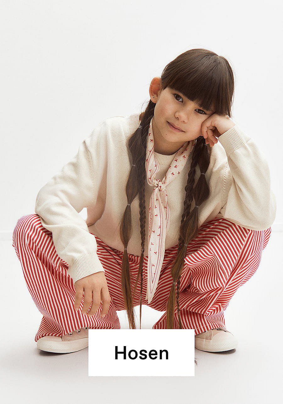 Mädchen mit Zöpfen, cremefarbenem Pullover, rot gestreifter Hose und Schal, das auf weißem Hintergrund hockt. Text: Unterteile.