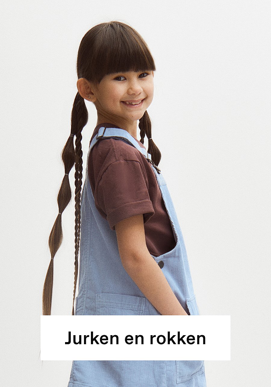 Lachend meisje met lange, bolle staartjes en een pony, gekleed in een bruin T-shirt en een lichtblauwe corduroy-overall. Tekst: Jurken en rokken
