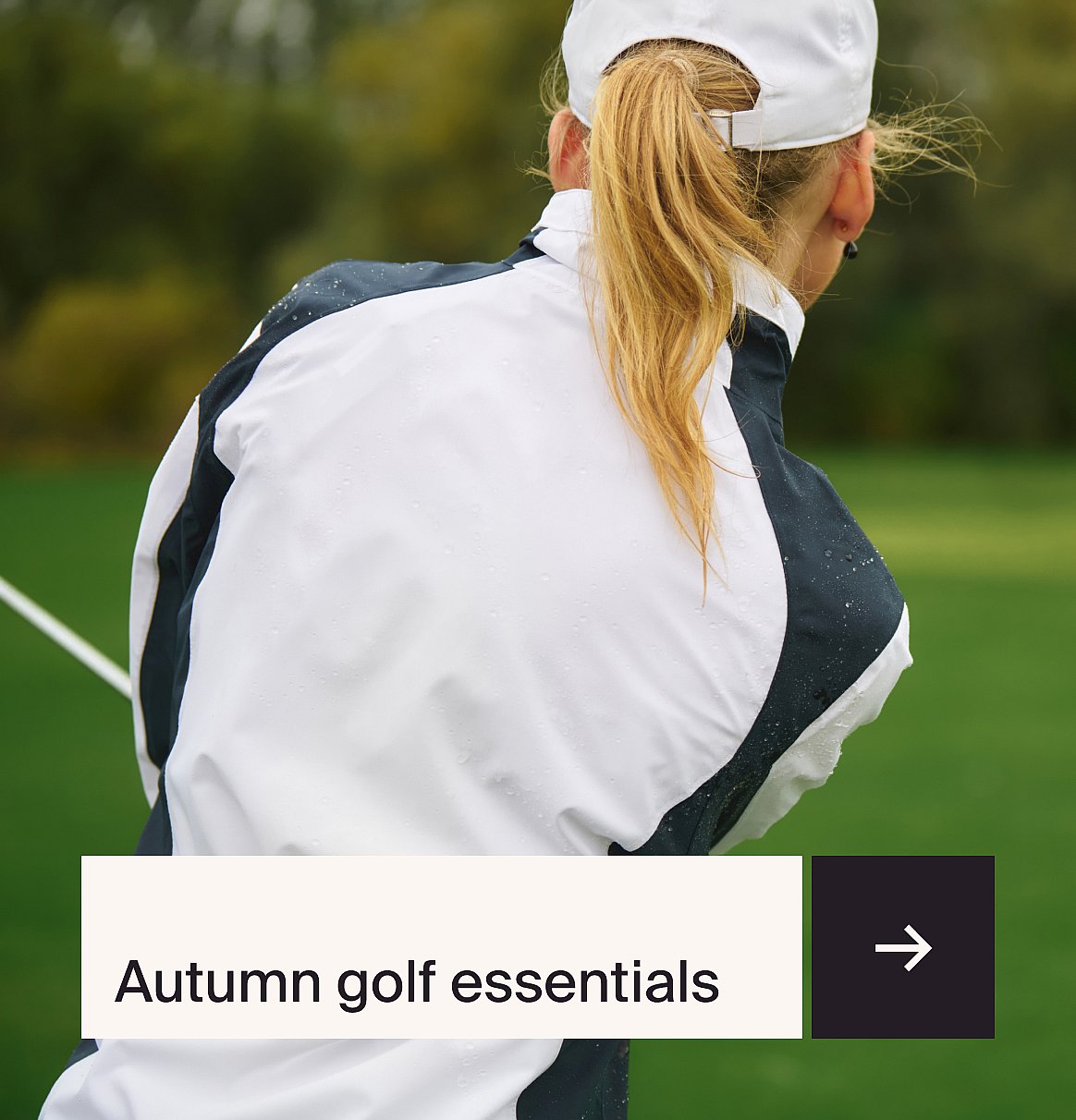 Woman golfer from behind, blonde ponytail, in a wet white and dark jacket on a green course. Text: Autumn golf essentials.