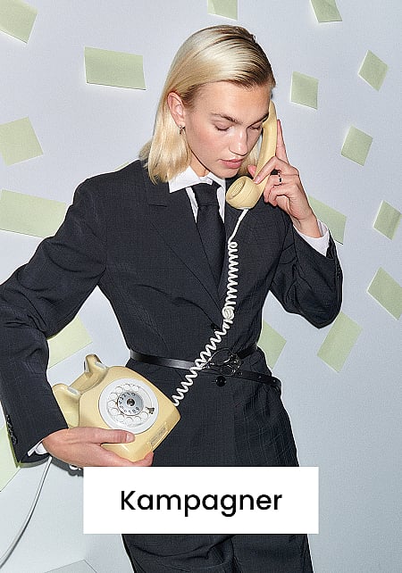 En person i mørkt jakkesæt og slips, der holder en beige drejetelefon op til øret, mens vedkommende holder basen i den anden hånd. Hvid væg. Tekst: Kampagner