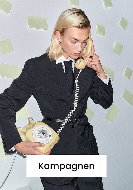 Eine Person in einem dunklen Anzug und mit Krawatte, die ein beiges Wählscheibentelefon ans Ohr hält, während sie die Basisstation in der anderen Hand hält. Weiße Wand. Text: Kampagnen
