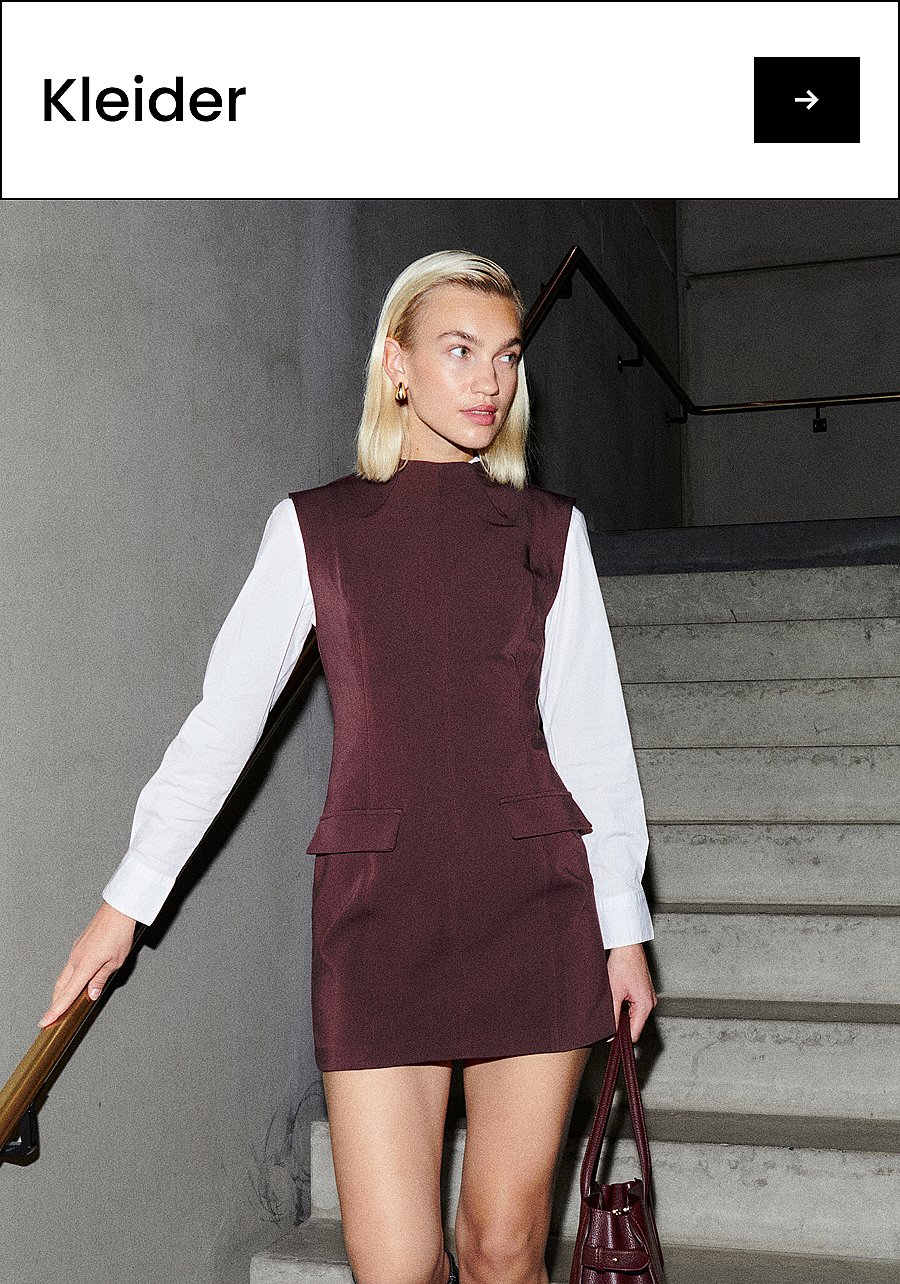 Blonde Frau in einem weinroten, ärmellosen Kleid über einem weißen Hemd, mit einer dazu passenden Tasche in der Hand, auf einer Betontreppe. Text: Kleider.