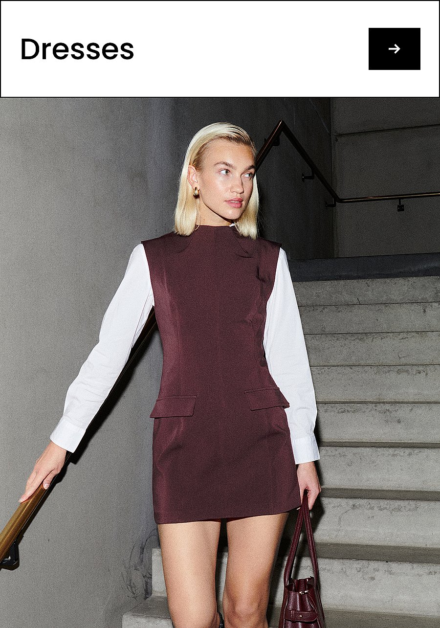 Blonde woman in maroon sleeveless dress over white shirt, holding a matching bag, on concrete stairs. Text: Dresses.