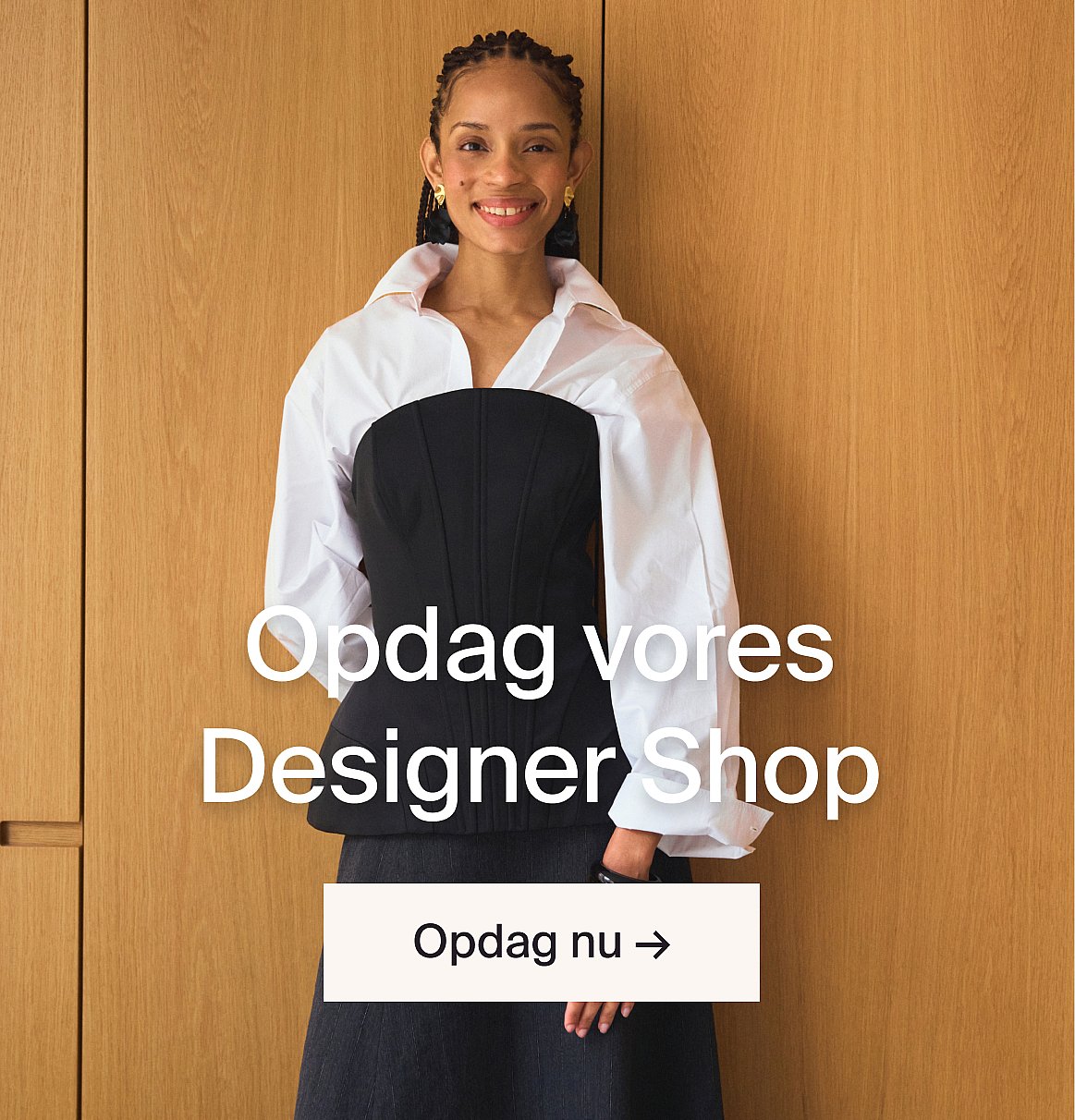 Smilende kvinde i sort korset og hvid skjorte mod træ. Tekst: Oplev vores designerbutik.