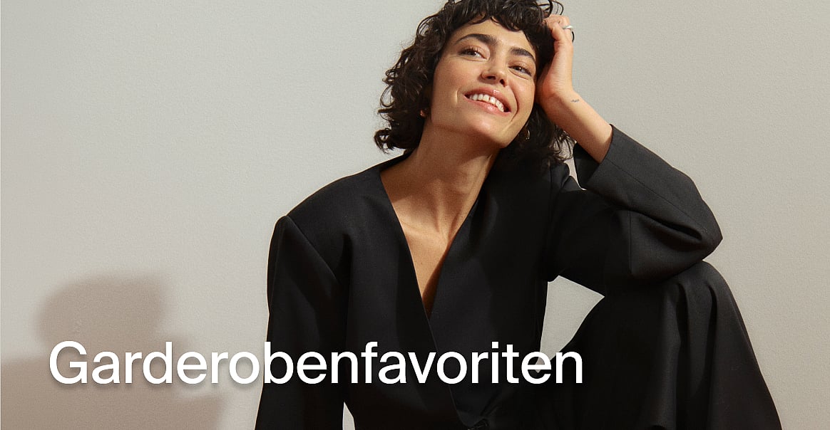 Lächelnde Frau in einem schwarzen Blazer, die Hand in ihrem lockigen Haar. Text: Grundausstattung.