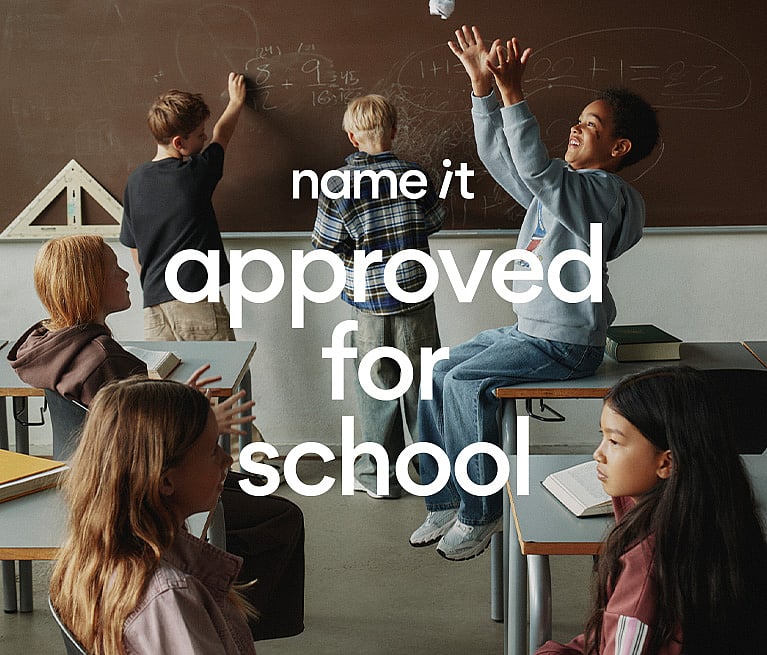 Children in a classroom. One boy throws paper, another writes on the blackboard. Text overlay: "name it approved for school".