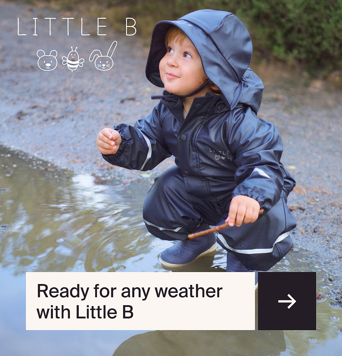Toddler in a dark blue hooded rain suit crouches by a puddle, holding a stick, looking up.