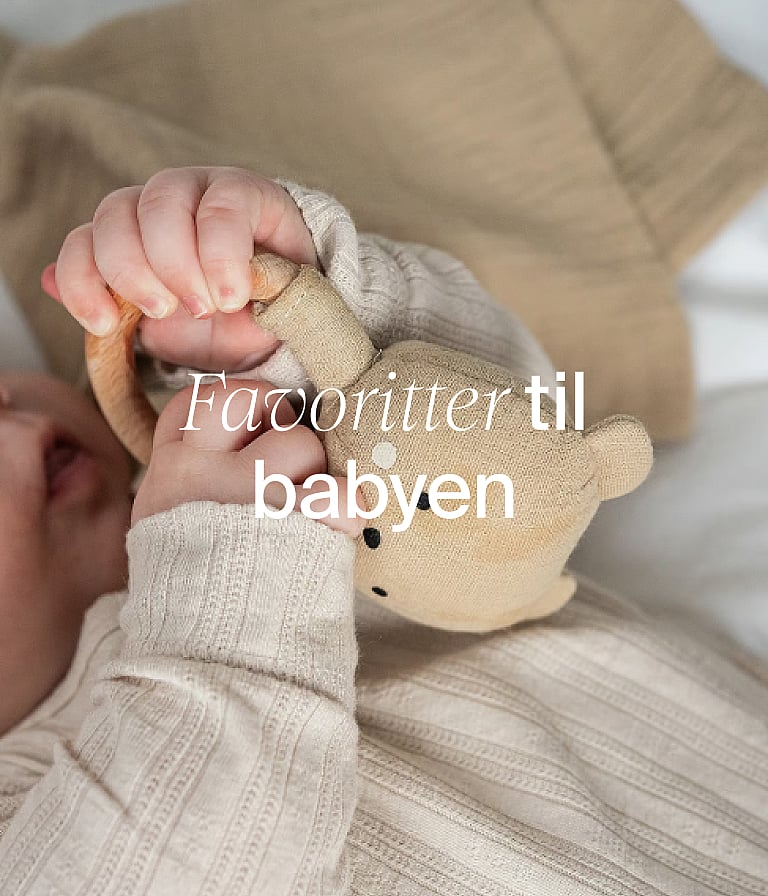 Et spædbarns hænder i neutralt tøj, der holder en bamse af stof. Tekst i billedet: »Nødvendigheder til babyen«.