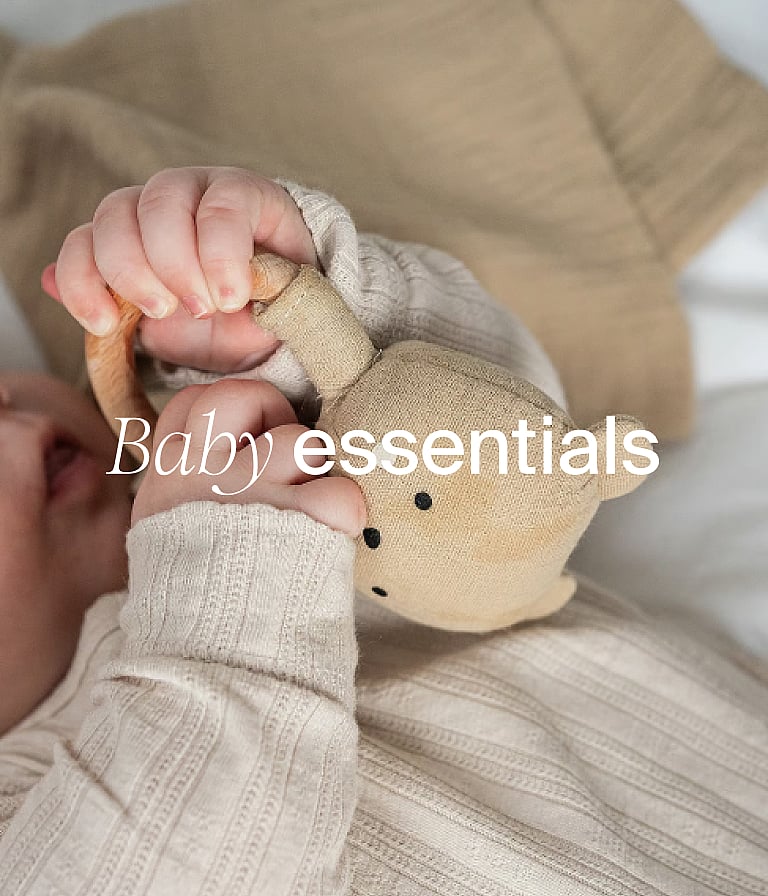 Baby's hands in neutral clothing holding a fabric bear toy. Text overlay: "Baby essentials".