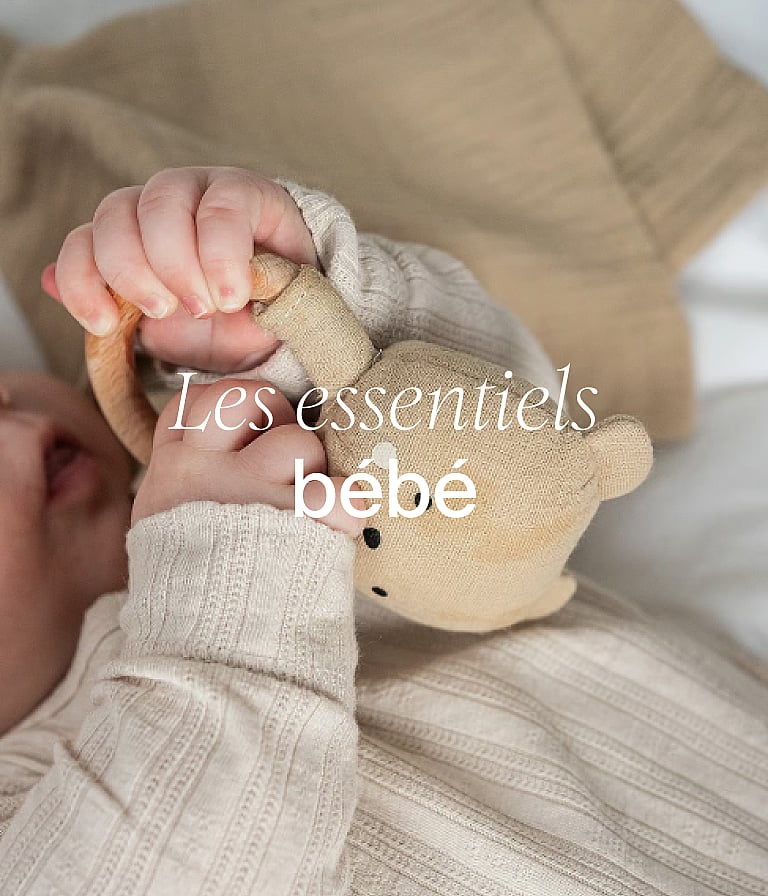 Les mains d'un bébé, vêtu de vêtements de couleur neutre, tenant un ours en peluche. Légende : « Les indispensables pour bébé ».