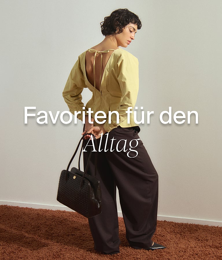 Frau in hellgelbem, rückenfreiem Oberteil und dunkler Hose, die eine schwarze Tasche in der Hand hält und auf einem braunen Teppich steht. Text: Alltägliche Favoriten.