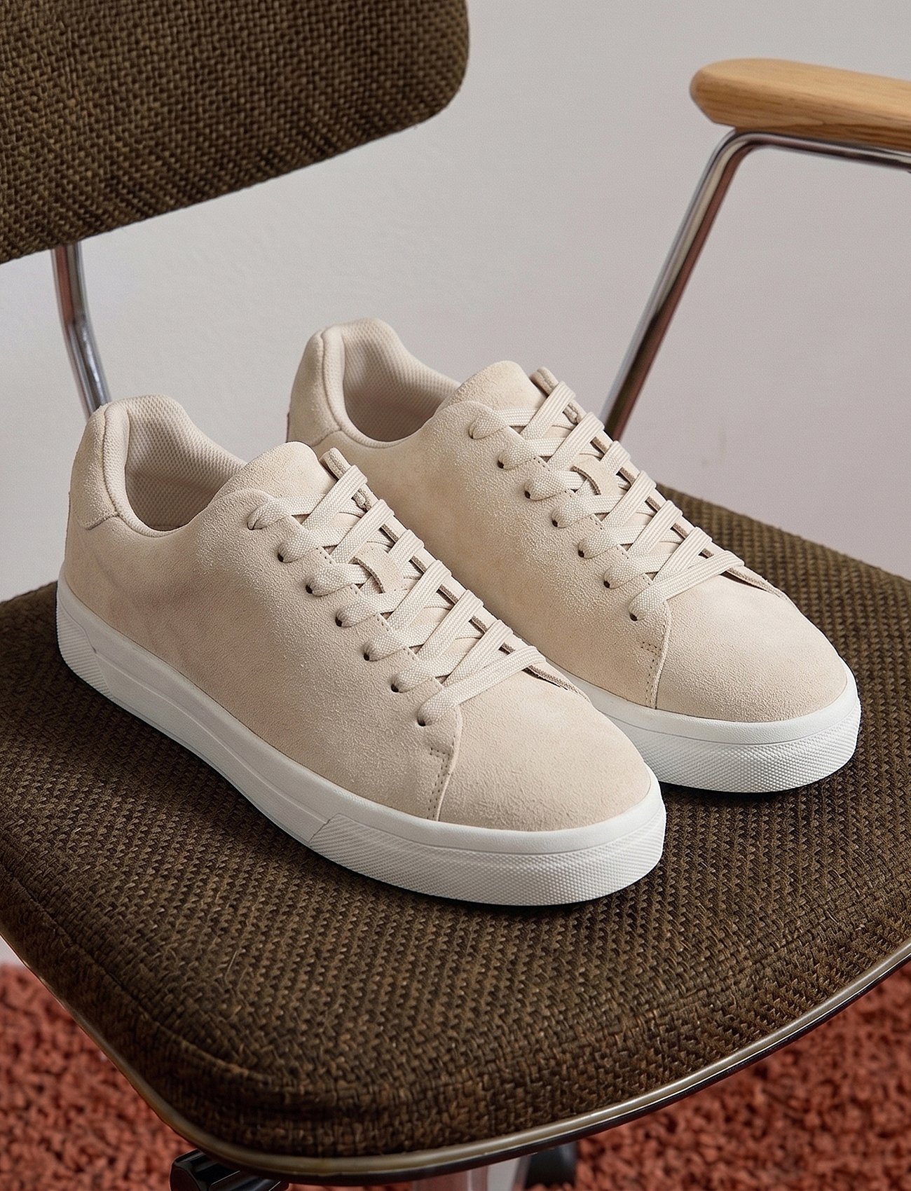 Light beige sneakers with white soles on a brown textured chair.