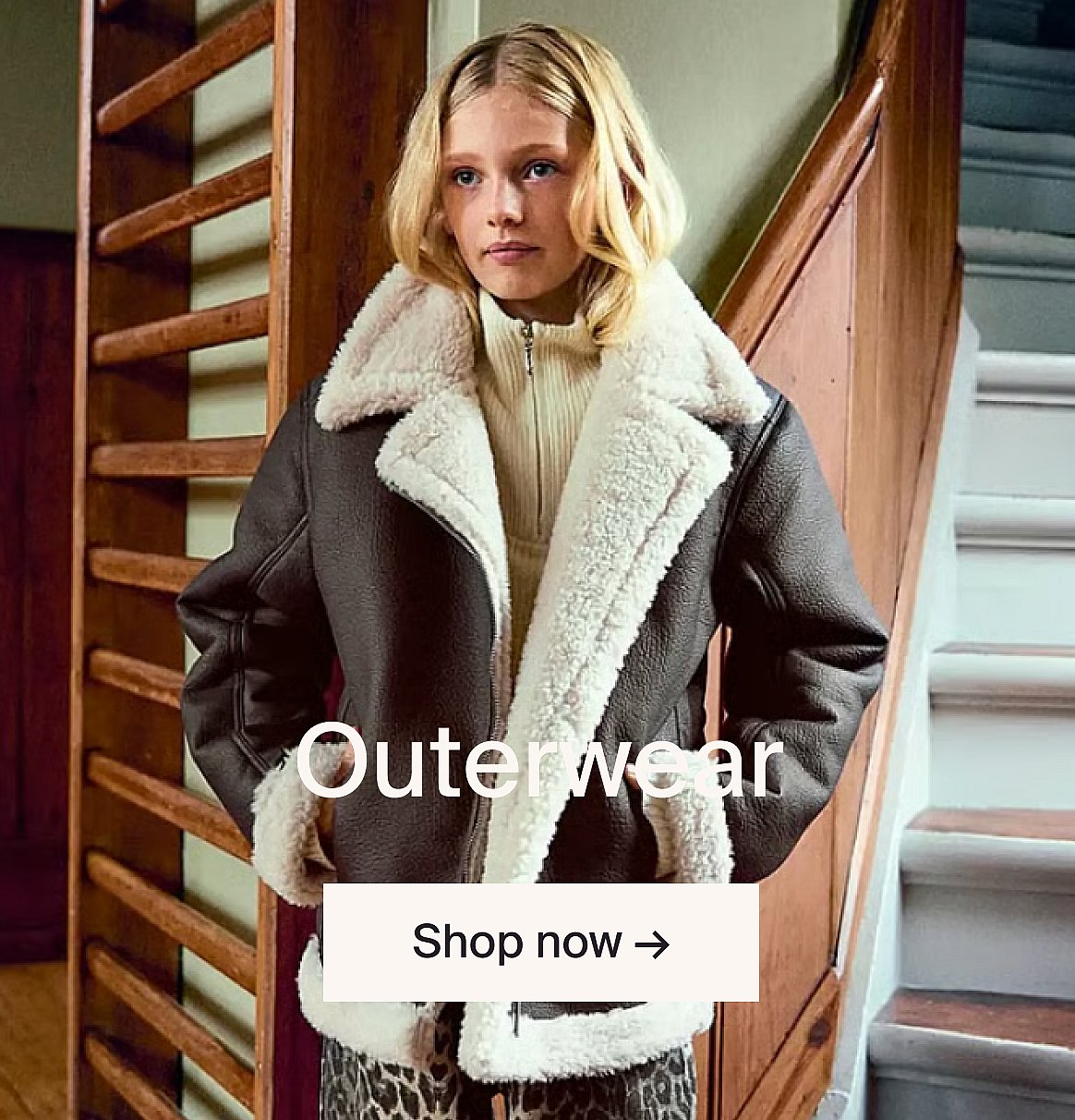 Child with braided hair in a tan jacket, looking up. Blue-grey background. Text: Outerwear, Shop now.