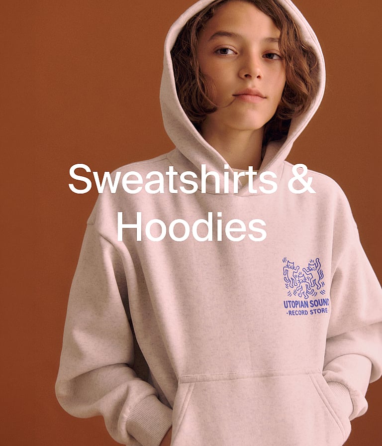 Young boy in a navy cap and beige sweatshirt and sweatpants. Text overlay: "Sweatshirts & Hoodies".