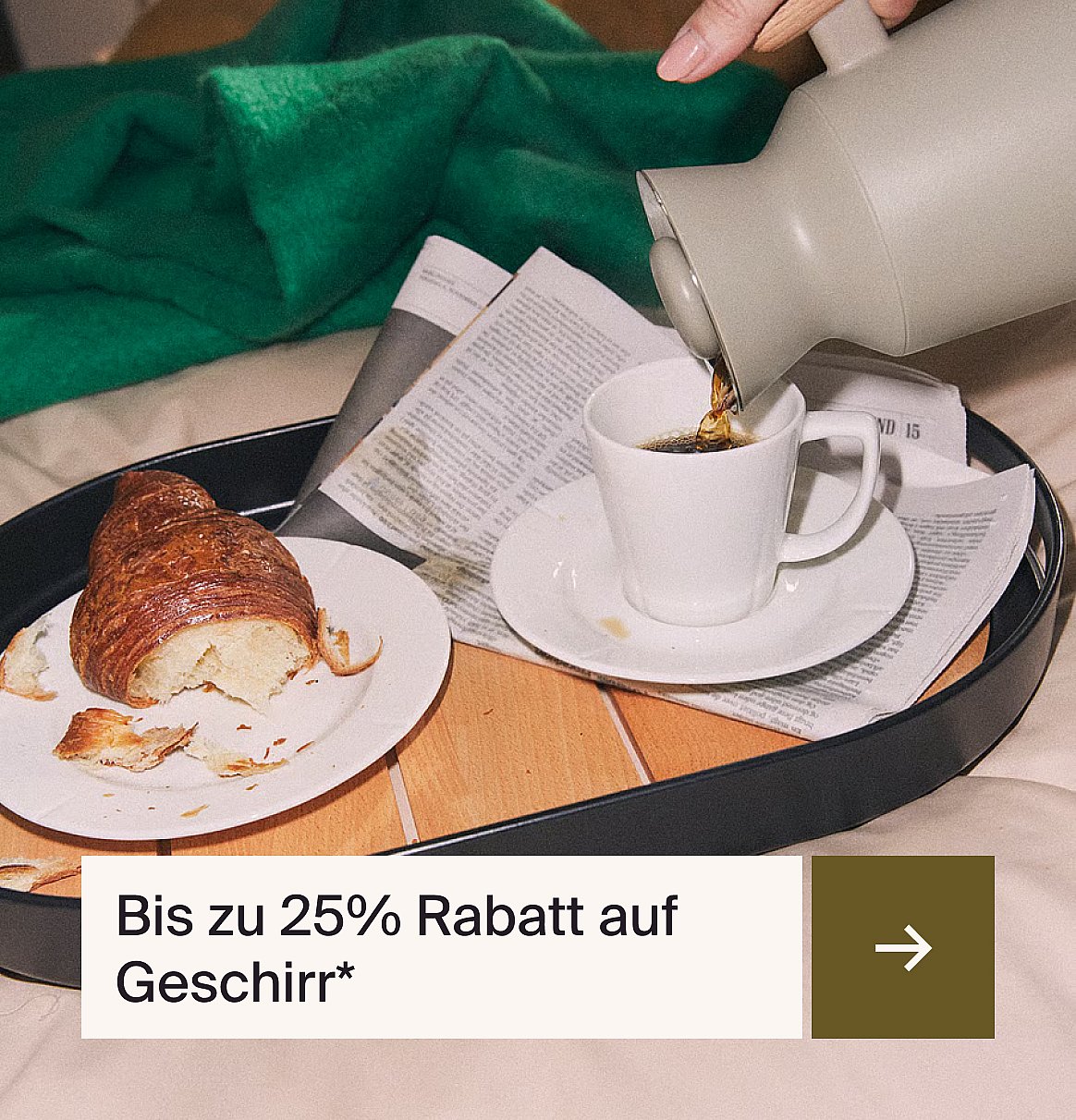 Kaffee wird von Hand in eine Tasse auf einem Tablett mit einem Croissant und einer Zeitung eingeschenkt. Grüne Decke. Text: Bis zu 25% auf Geschirr*.