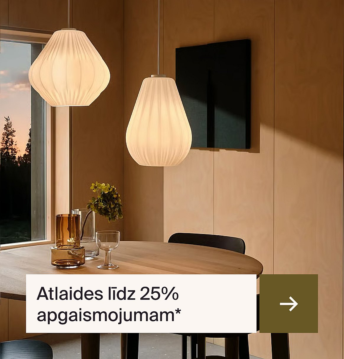 Divi moderni plisēti balti piekaramie gaismekļi krēslā apgaismo ēdamistabu ar koka galdu, krēsliem un logu.