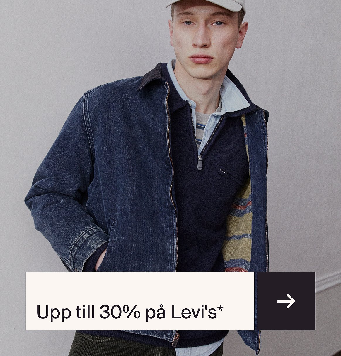En ung man i jeansjacka, tröja och keps, framför en enfärgad vägg. Text: ”Upp till 30% rabatt på Levi’s*”