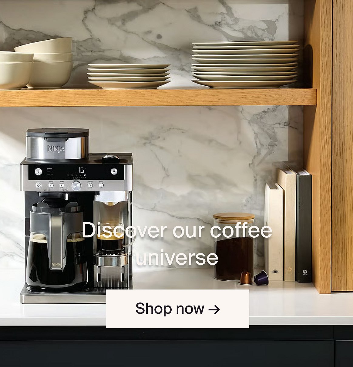Ninja coffee maker brewing coffee on a kitchen counter. Marble backsplash, wooden shelves with bowls and plates.