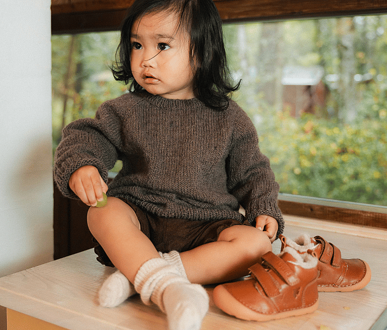 Skateboard leaning on a concrete bench, surrounded by six pairs of Puma suede sneakers in brown, orange, and black on