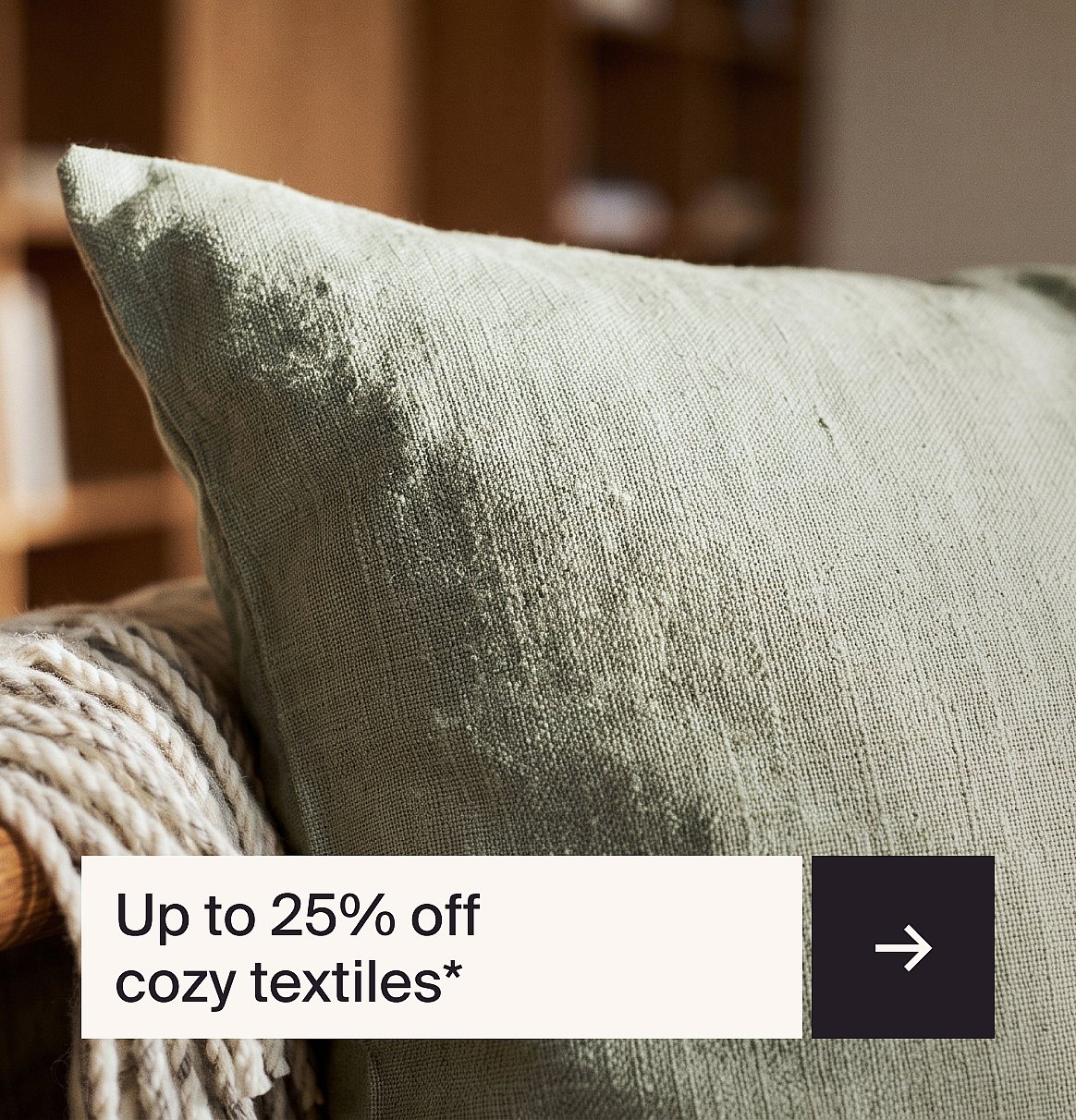 Light green textured pillow on a chair with a blanket. Text: Up to 25% off cozy textiles*.