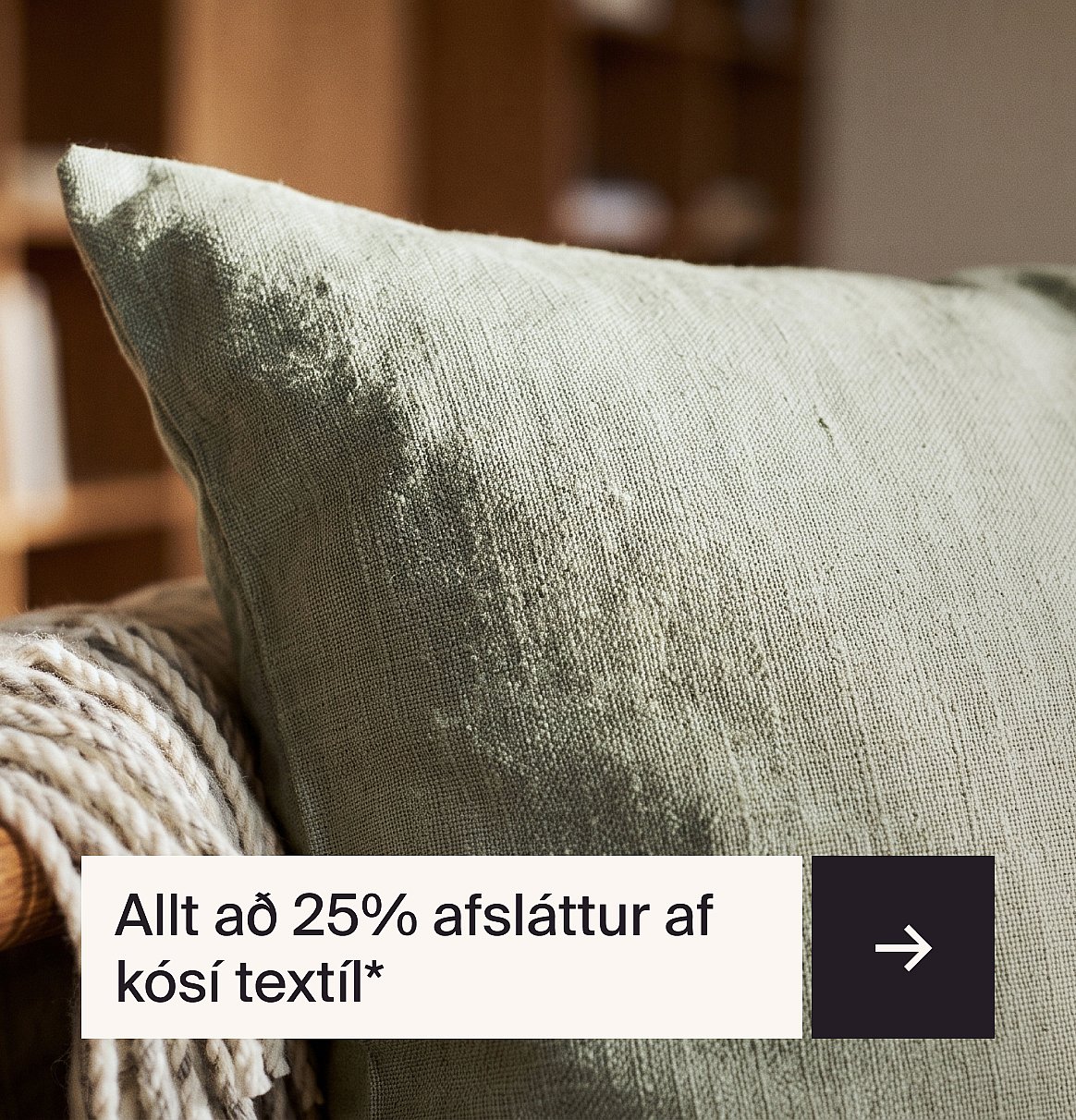 Ljósgrænn áferðarríkur koddi á stól með teppi. Texti: allt að 25% afsláttur af hlýjum textílum*.