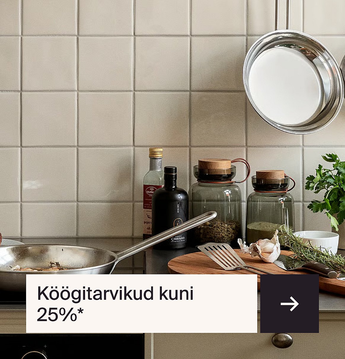 Köögitöölaud, millel on praepann, toiduõlid, vürtsipurgid, küüslauk, maitsetaimed ja plaaditud seinakate. Tekst: „Kuni 25% soodustust köögitarvetele“