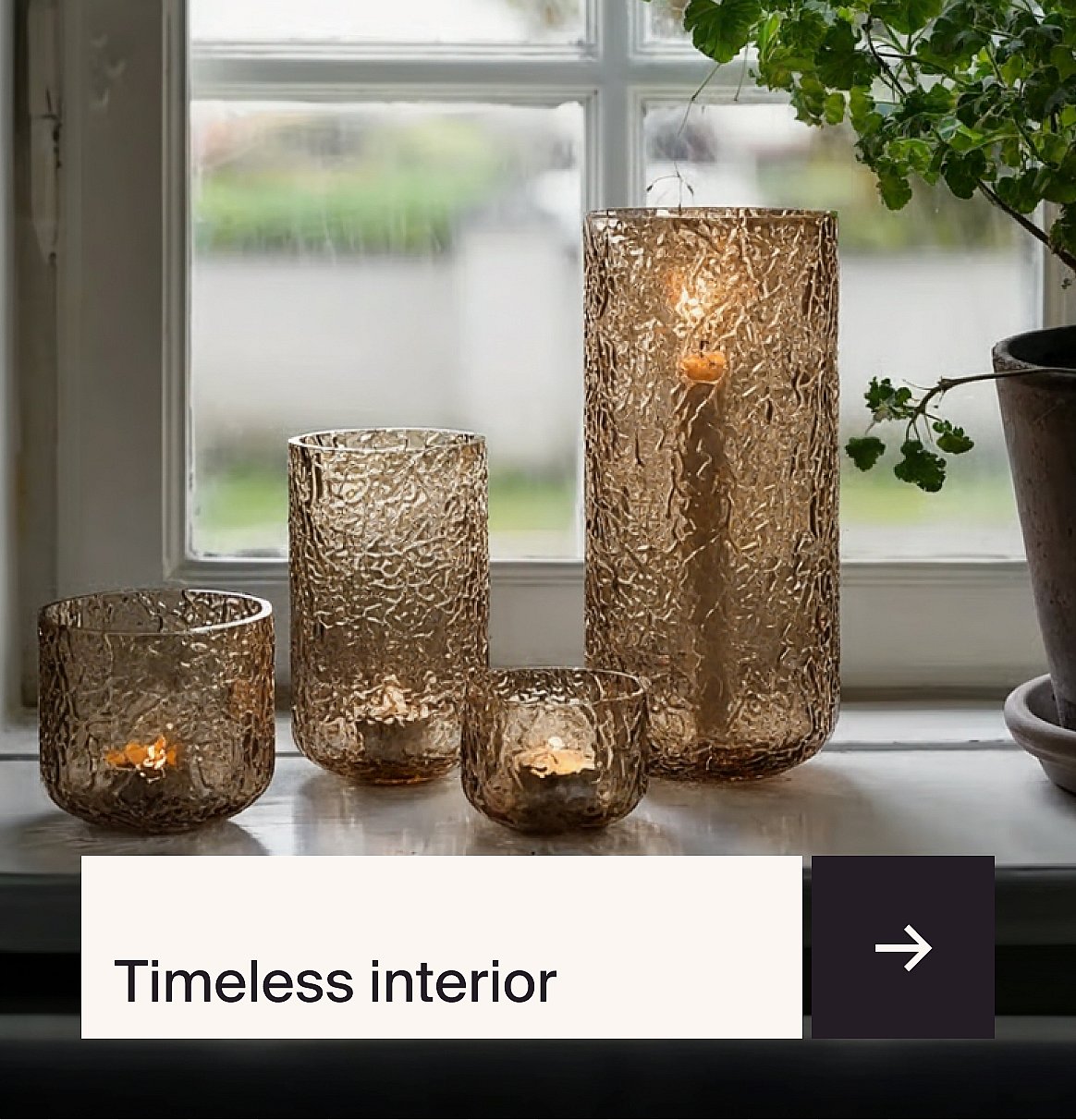 Four textured amber glass candle holders with lit candles on a windowsill, a plant on the right.