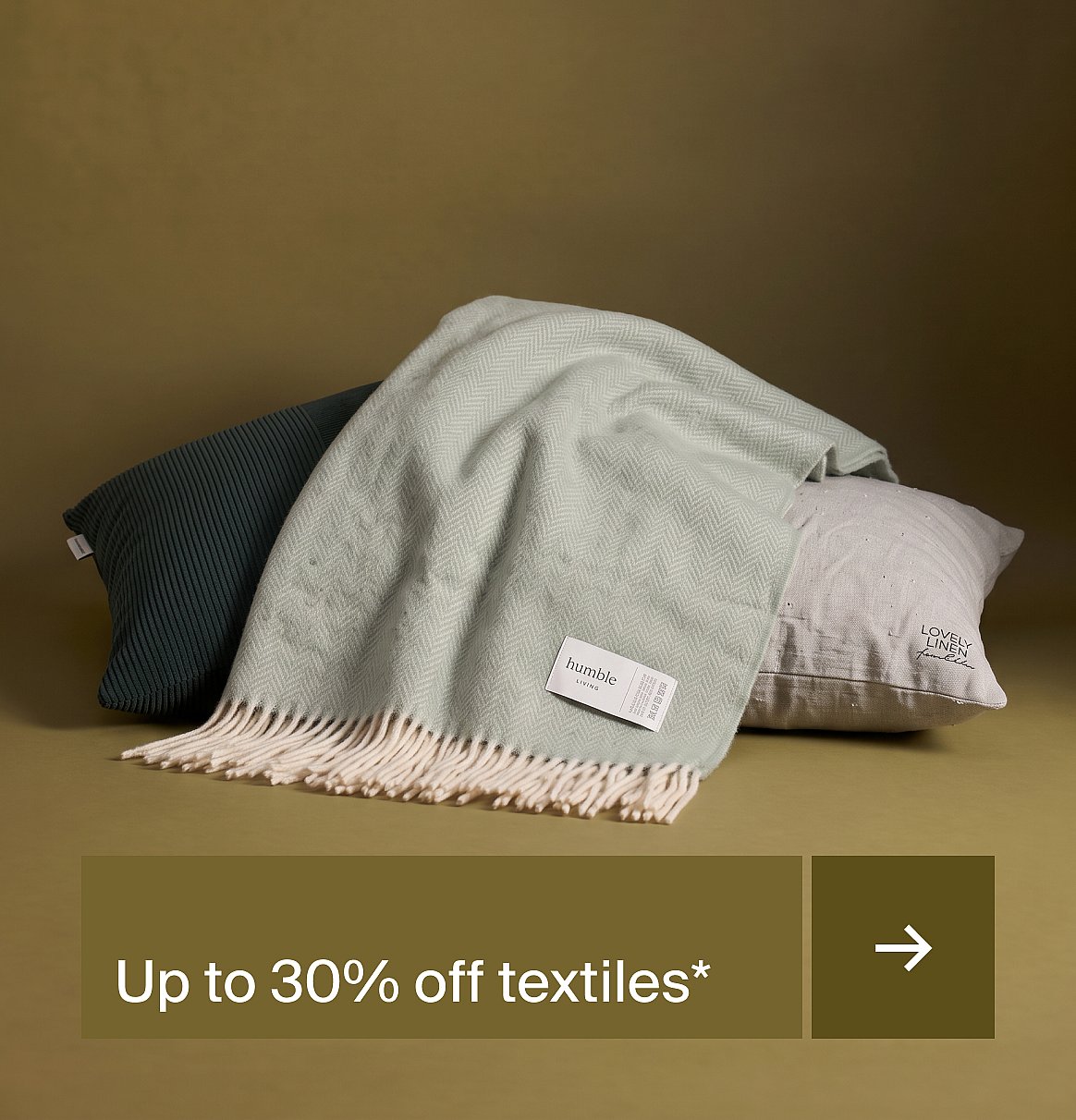 Dark green ribbed pillow, light green herringbone throw with fringe, and a beige pillow on an olive background.